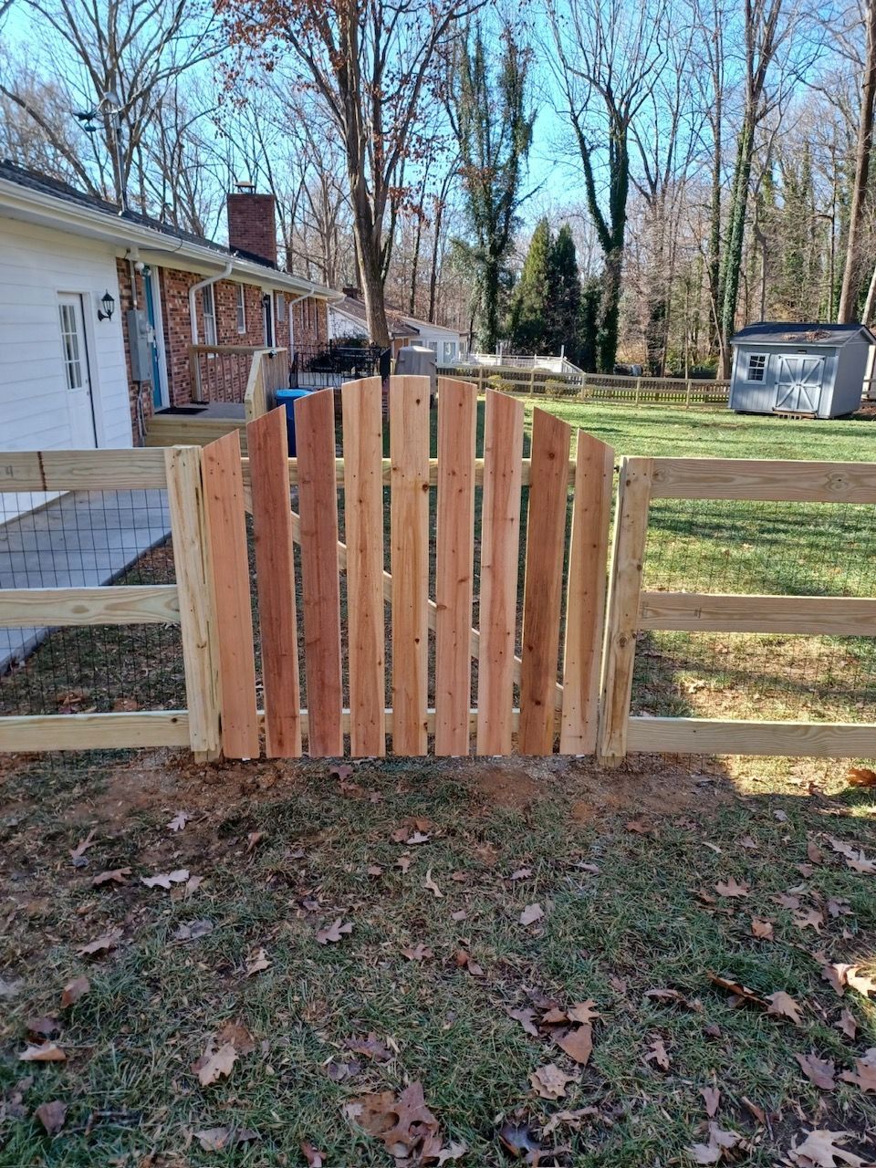 Wooden gate arching upwards, between two split-rail fences in a yard.