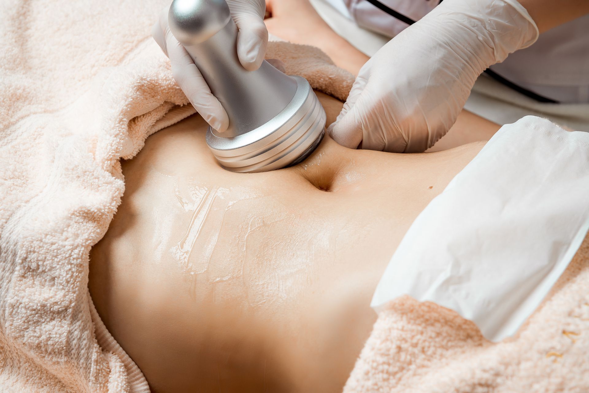 Person receiving body sculpting treatment on abdomen with gloved hands and device.