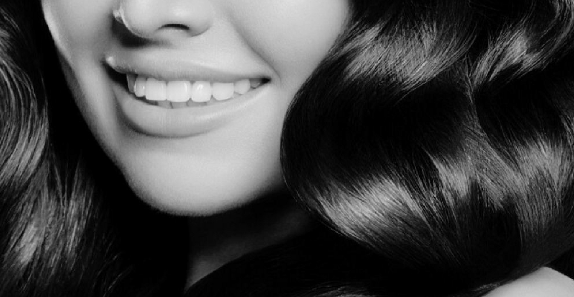 A woman with long hair is smiling in a black and white photo.