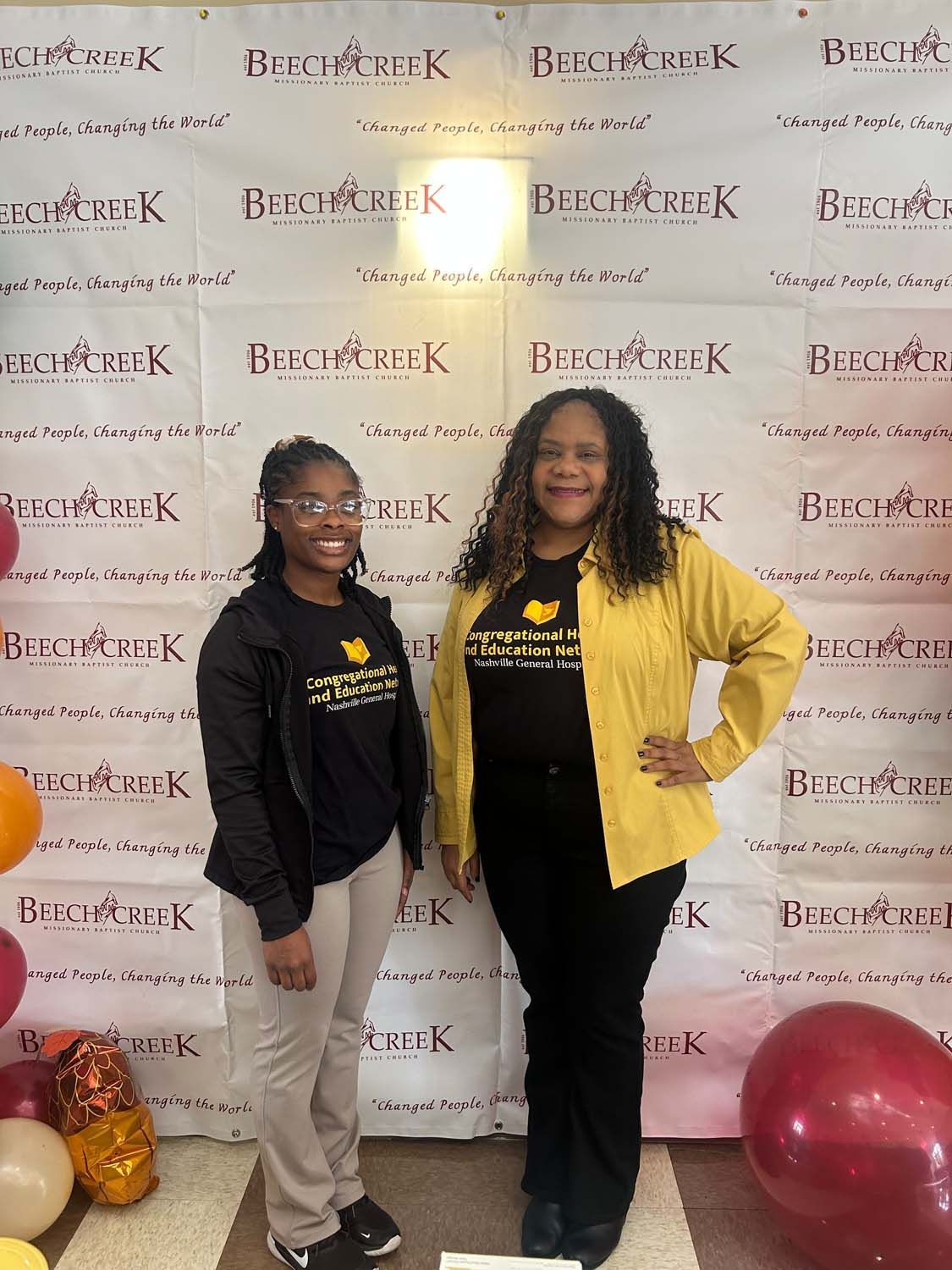 Two people pose in front of a branded 