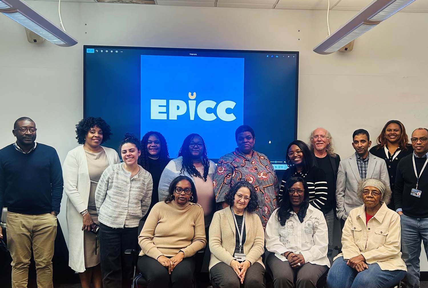 A group of fifteen professionals posing in front of a digital screen with the blue logo 