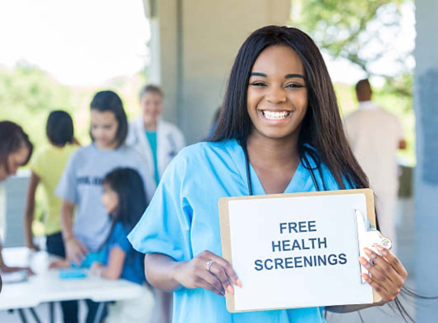 A smiling person in blue scrubs holding a sign that says 
