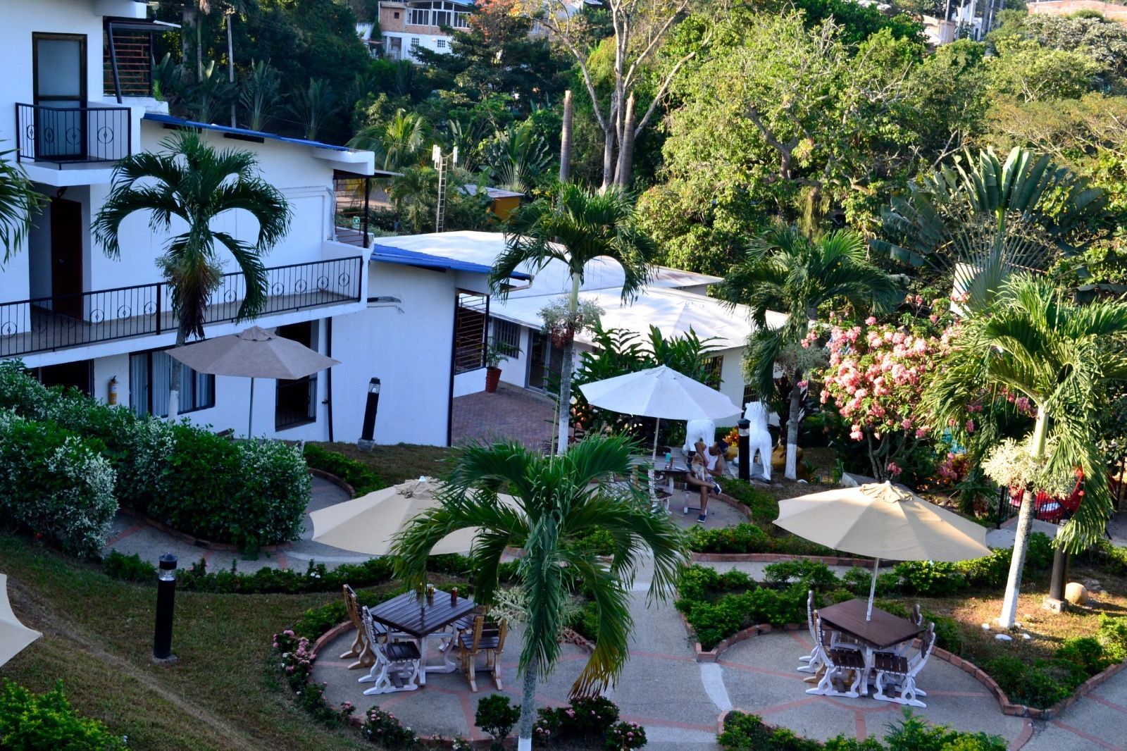 Edificios blancos y jardines con mesas, sombrillas y palmeras.