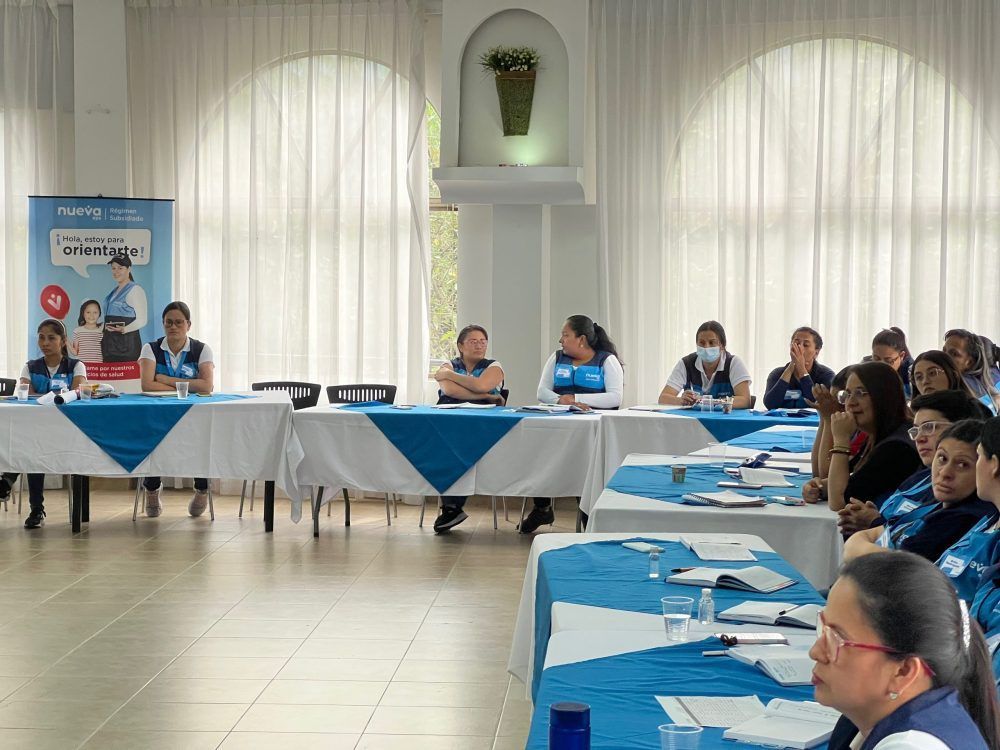 Las personas sentadas a las mesas en una sala decorada en azul y blanco parecen estar en una reunión.