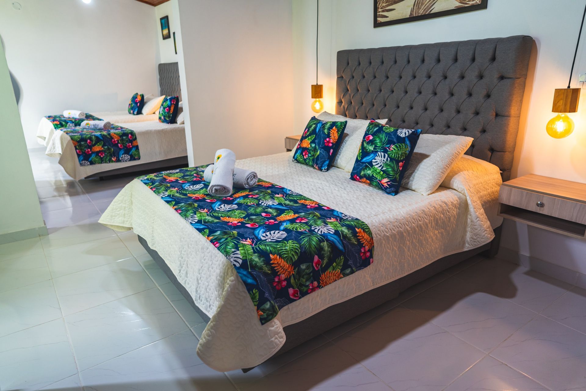 Dormitorio con una cama grande, cojines decorativos y una segunda cama reflejada en el espejo.