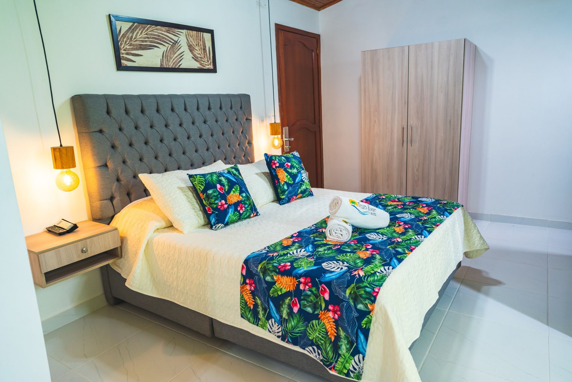 Dormitorio con cama, ropa de cama con estampado floral, cabecero capitoné, mesita de noche y armario.