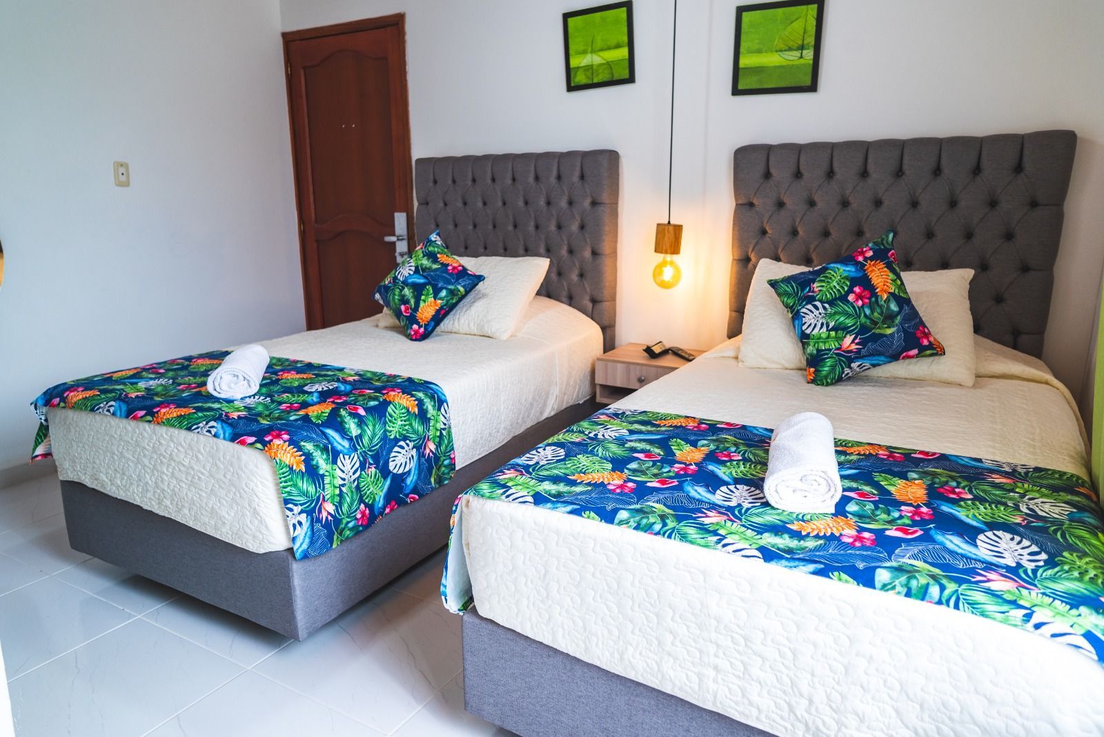 Dos camas individuales en una habitación con cabeceros grises y ropa de cama estampada en azul y verde.