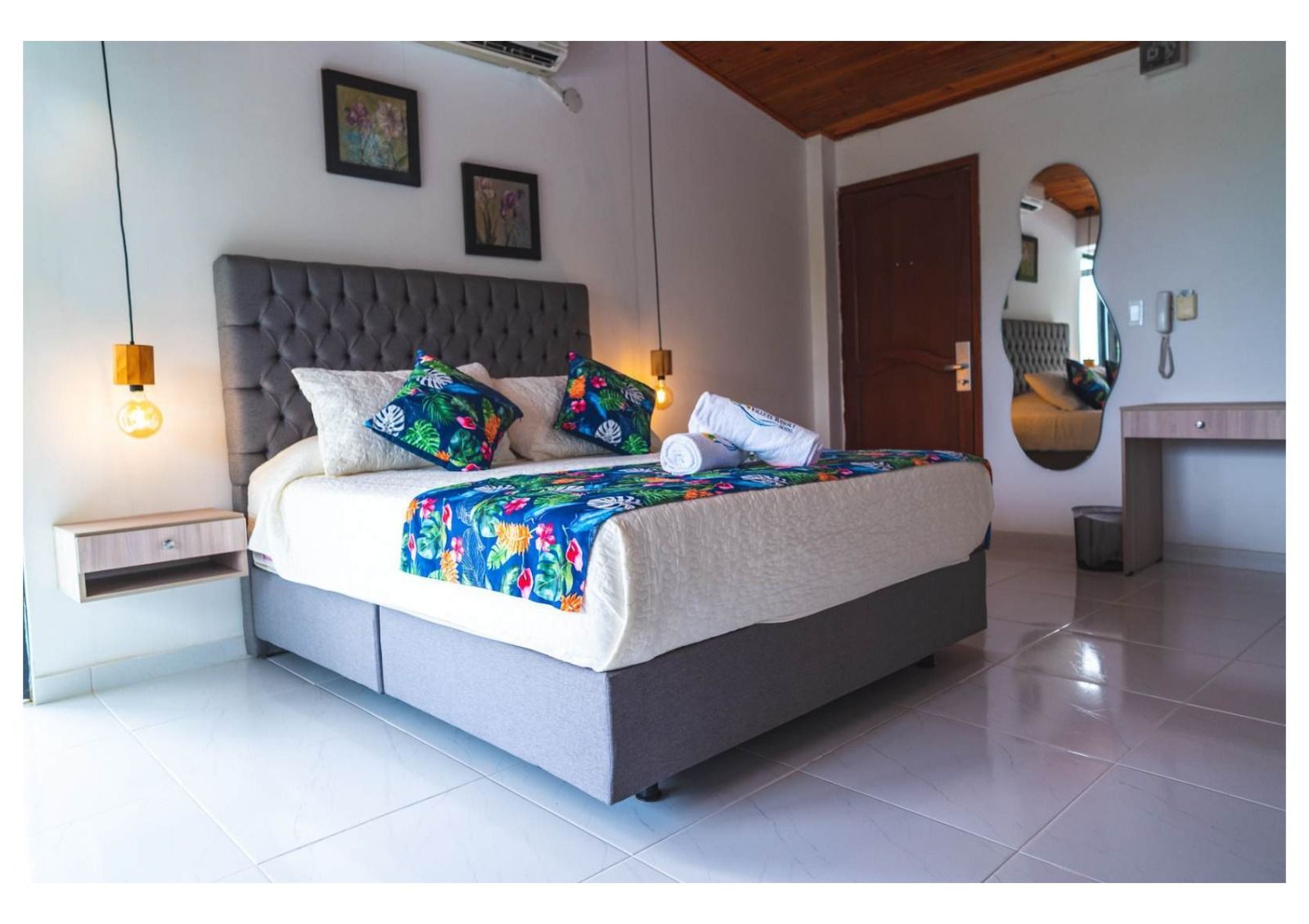 Dormitorio con cama gris, cabecero capitoné, ropa de cama estampada, detalles de madera y mesitas de noche.