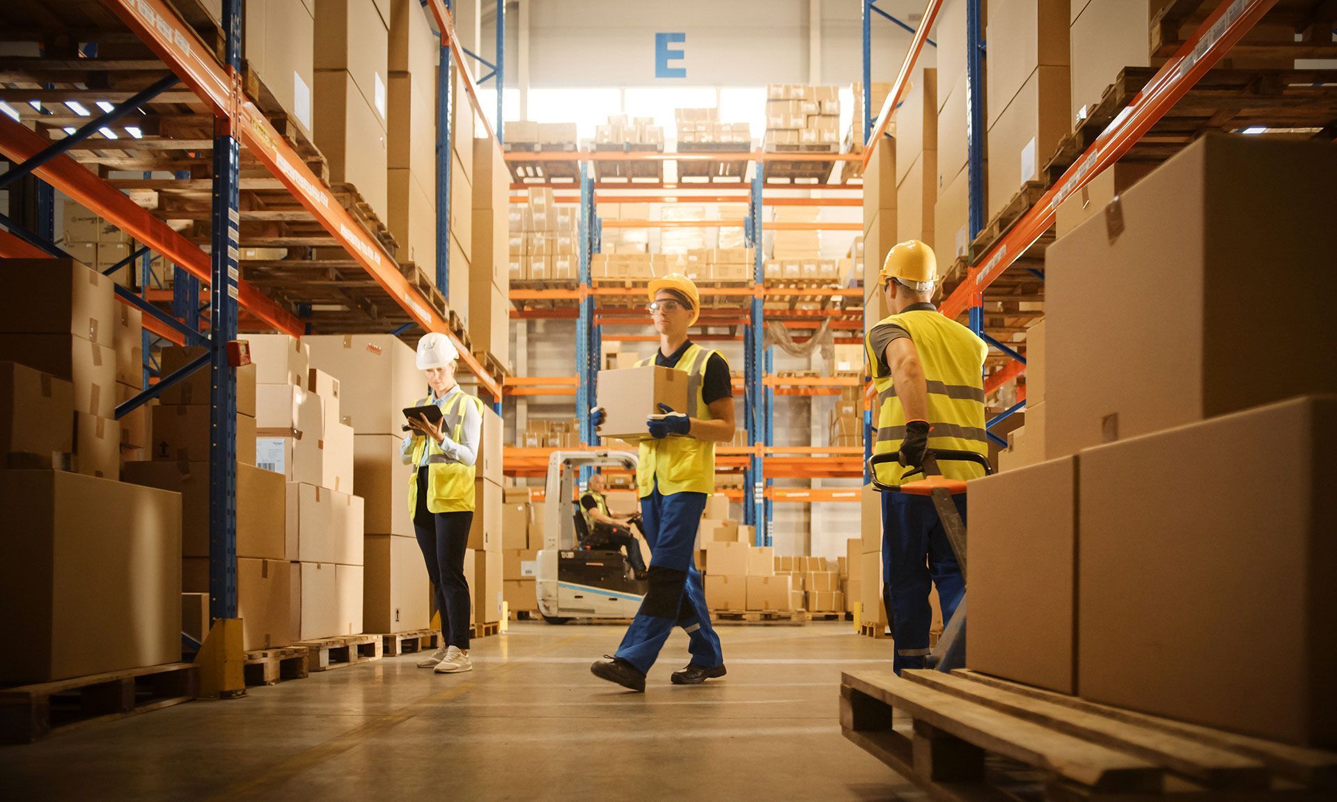Warehouse workers with boxes, shelves, and a forklift. Yellow vests, indoor setting.