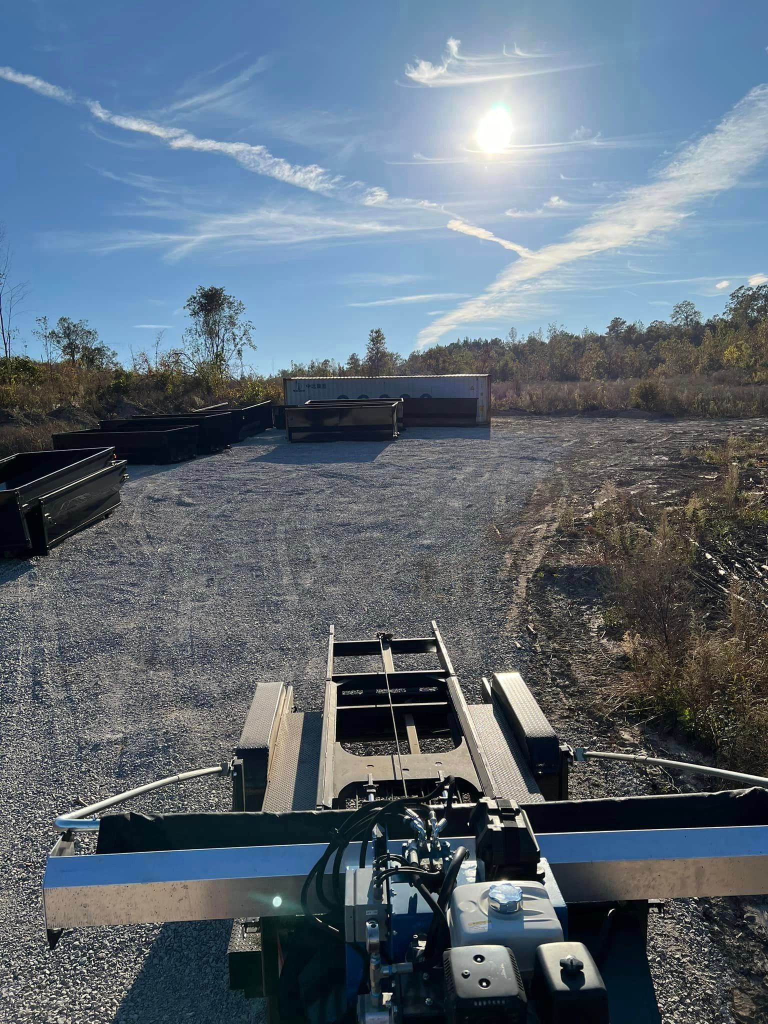 A truck is parked in a gravel lot with the sun shining through the clouds.