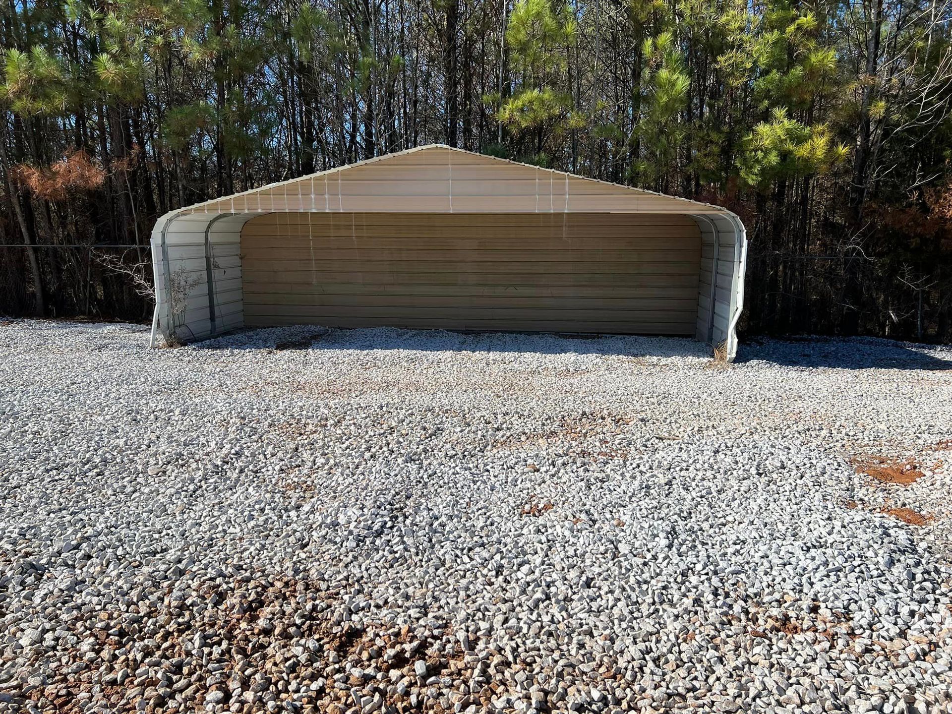 A garage is sitting in the middle of a gravel driveway.