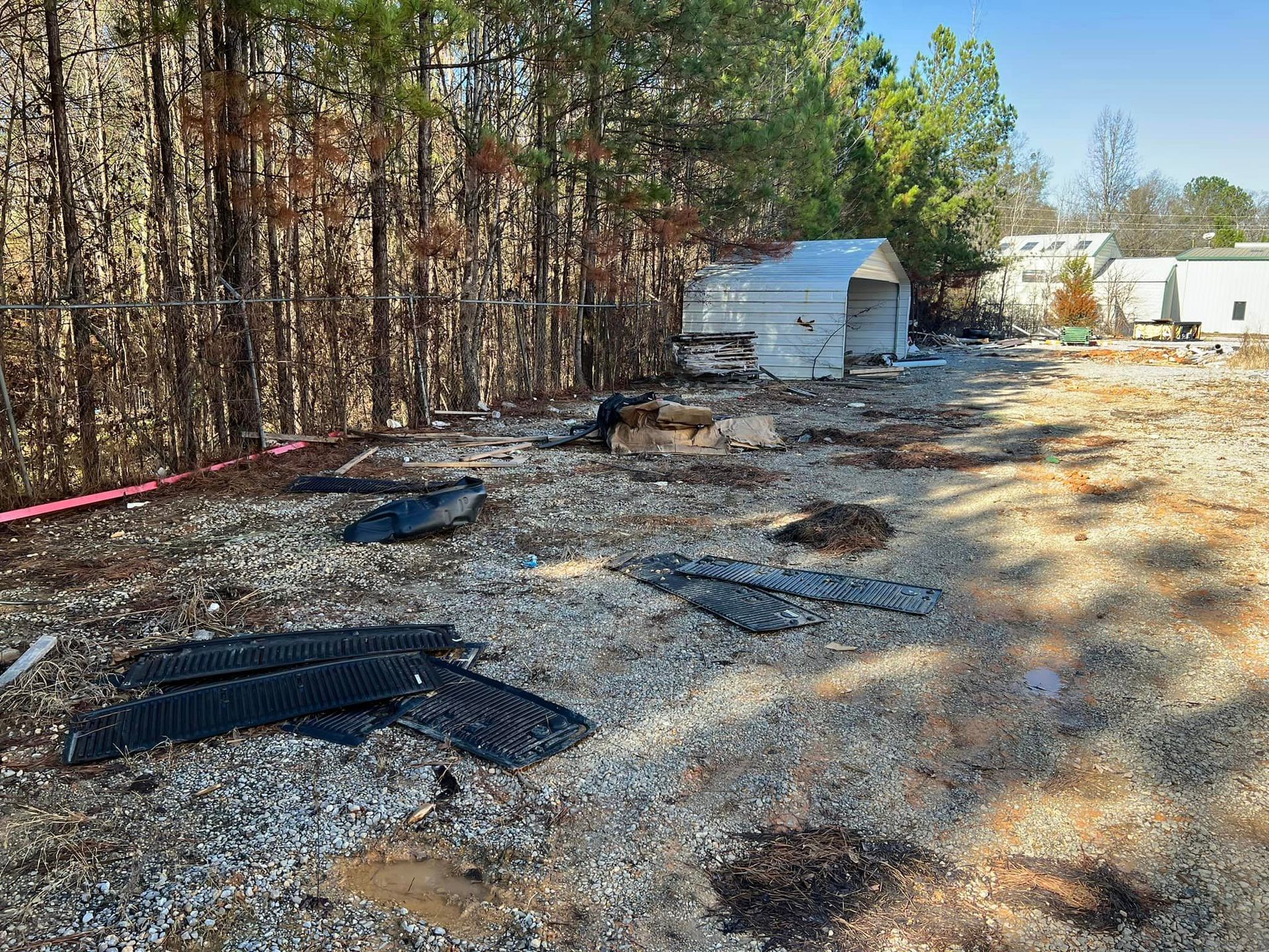 A shed is sitting in the middle of a dirt field surrounded by trees.