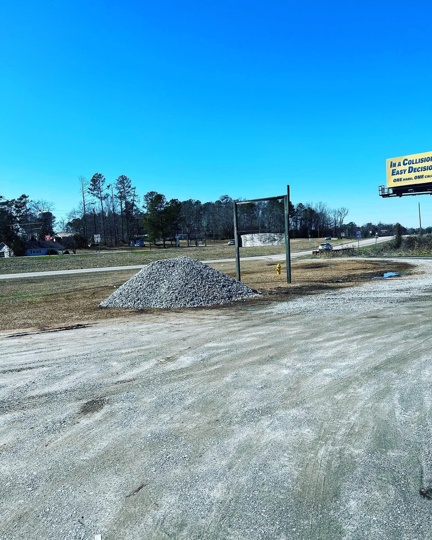 A dirt road with a pile of rocks in the middle and a billboard in the background