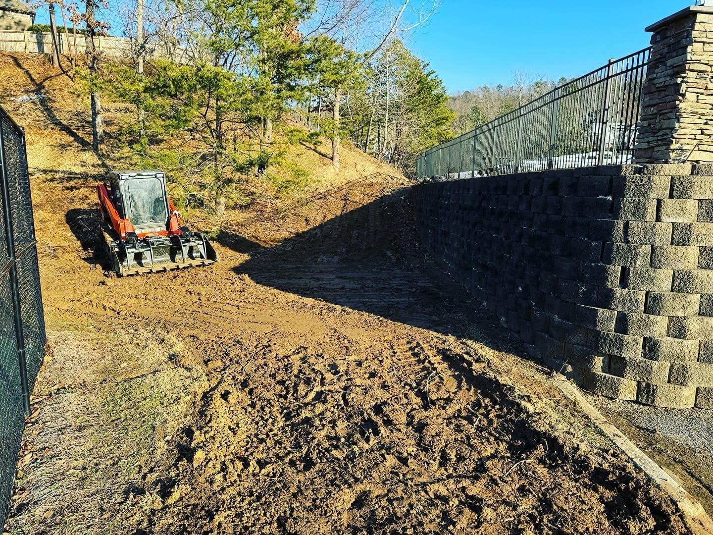 A bulldozer is working on a dirt road next to a fence.