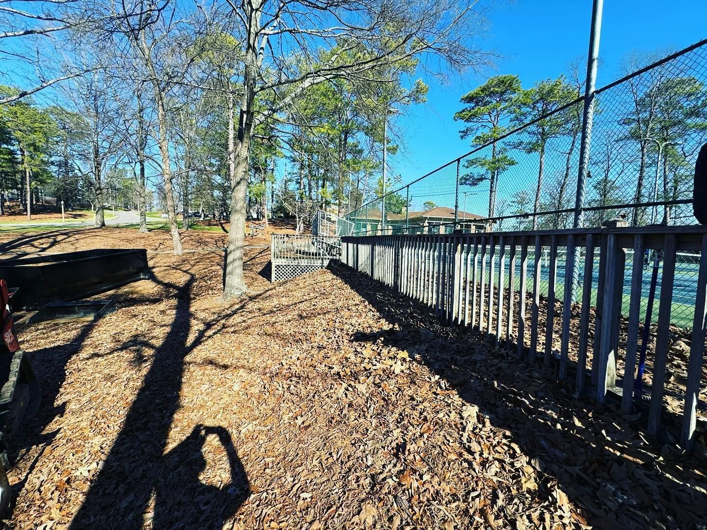 A shadow of a person is cast on the ground near a fence.