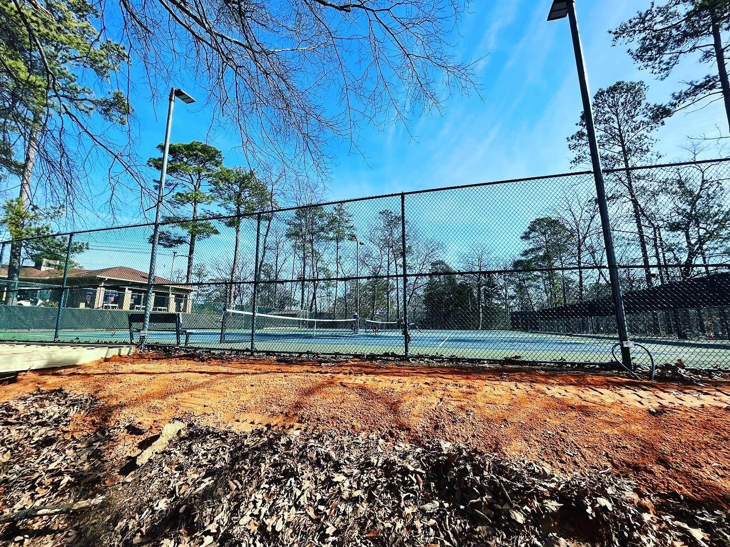 A tennis court with a fence around it and trees in the background.