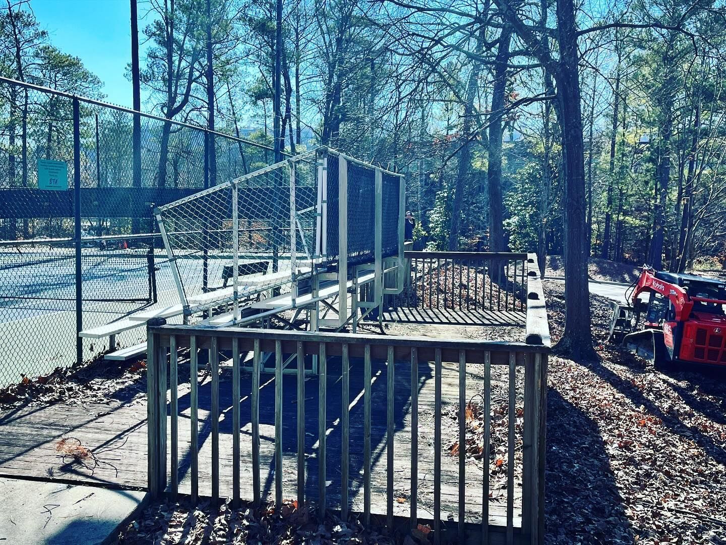 A fence surrounds a tennis court in the woods