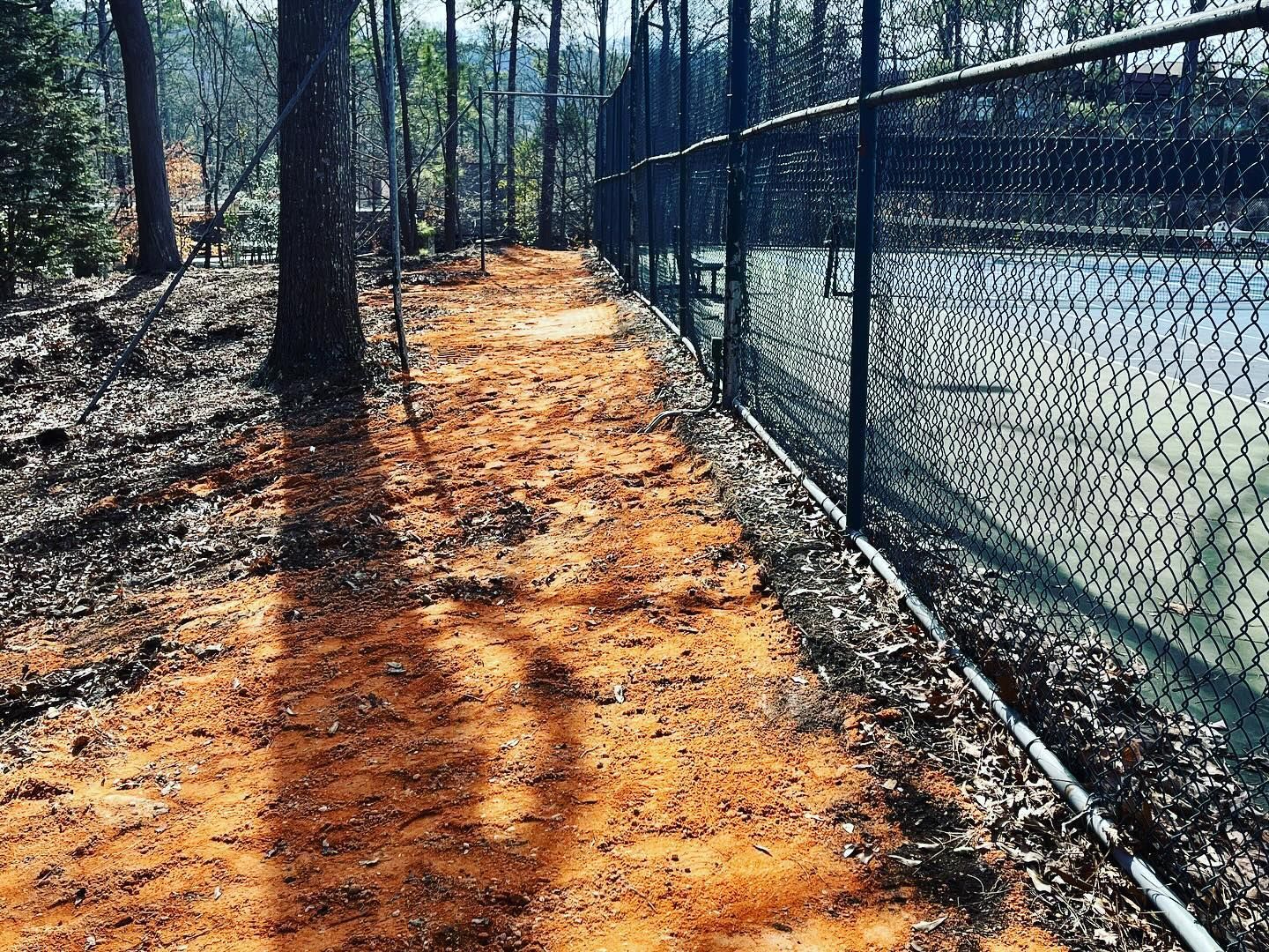 A chain link fence surrounds a tennis court in the woods.