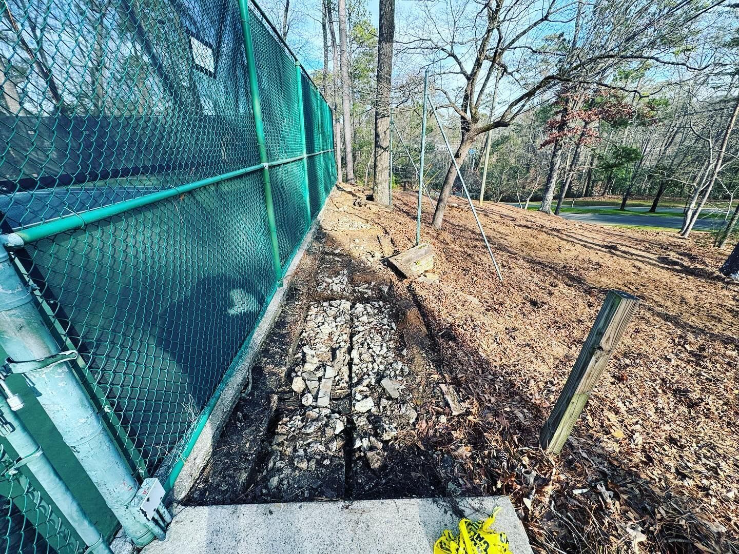 A green chain link fence is surrounded by trees and leaves in a park.