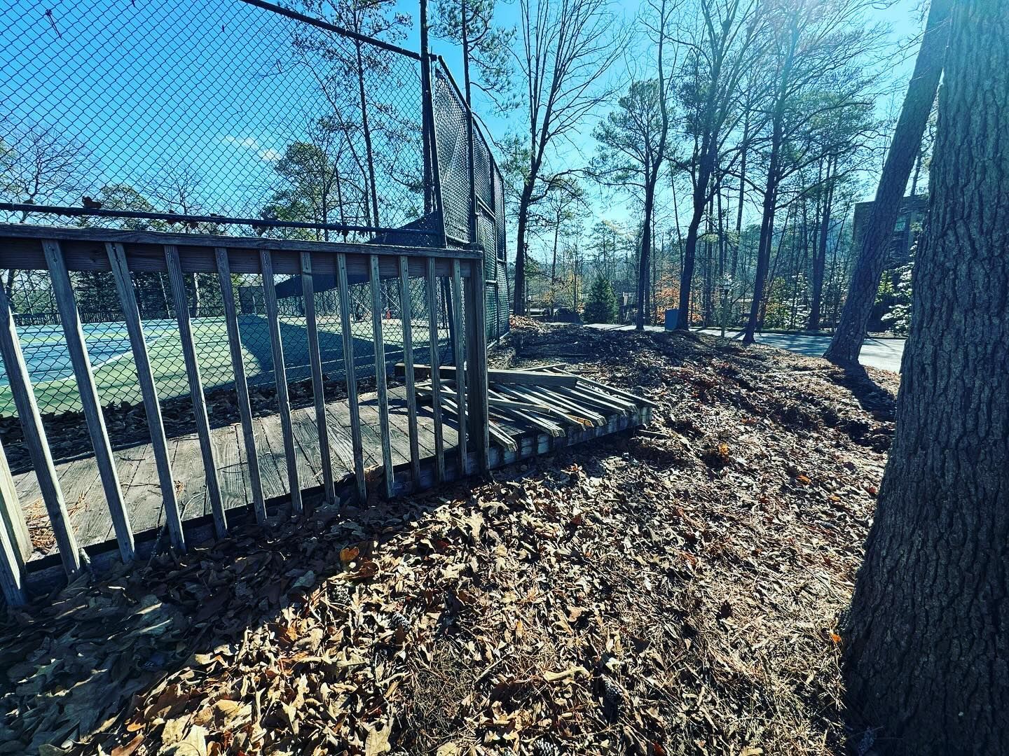 A chain link fence is surrounded by trees and leaves in a park.
