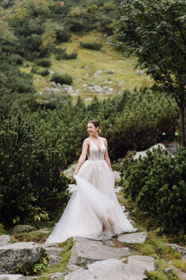 A bride in a wedding dress is standing on a path in the mountains.