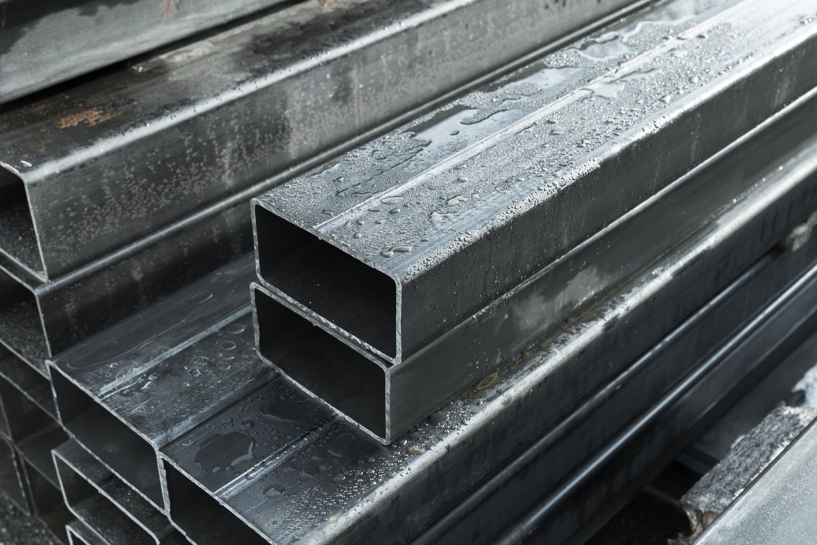 Stacks of rectangular steel tubes, wet with condensation.