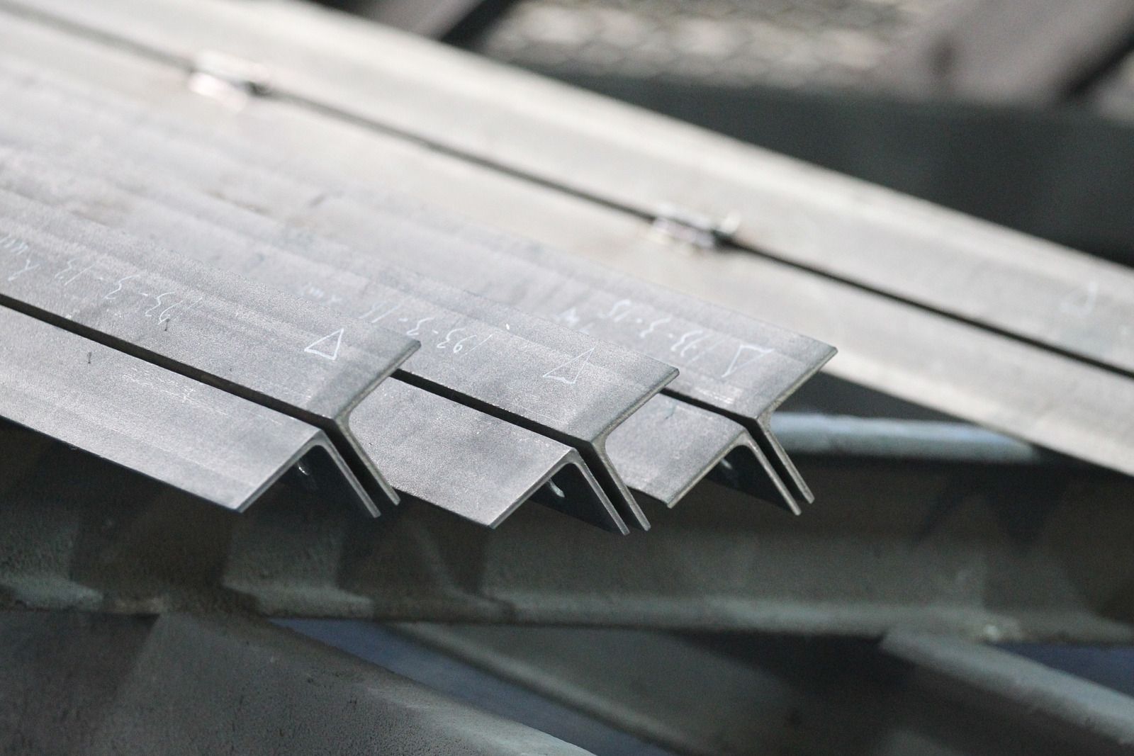 Angle steel beams, in a pile, with a gray, metallic appearance.