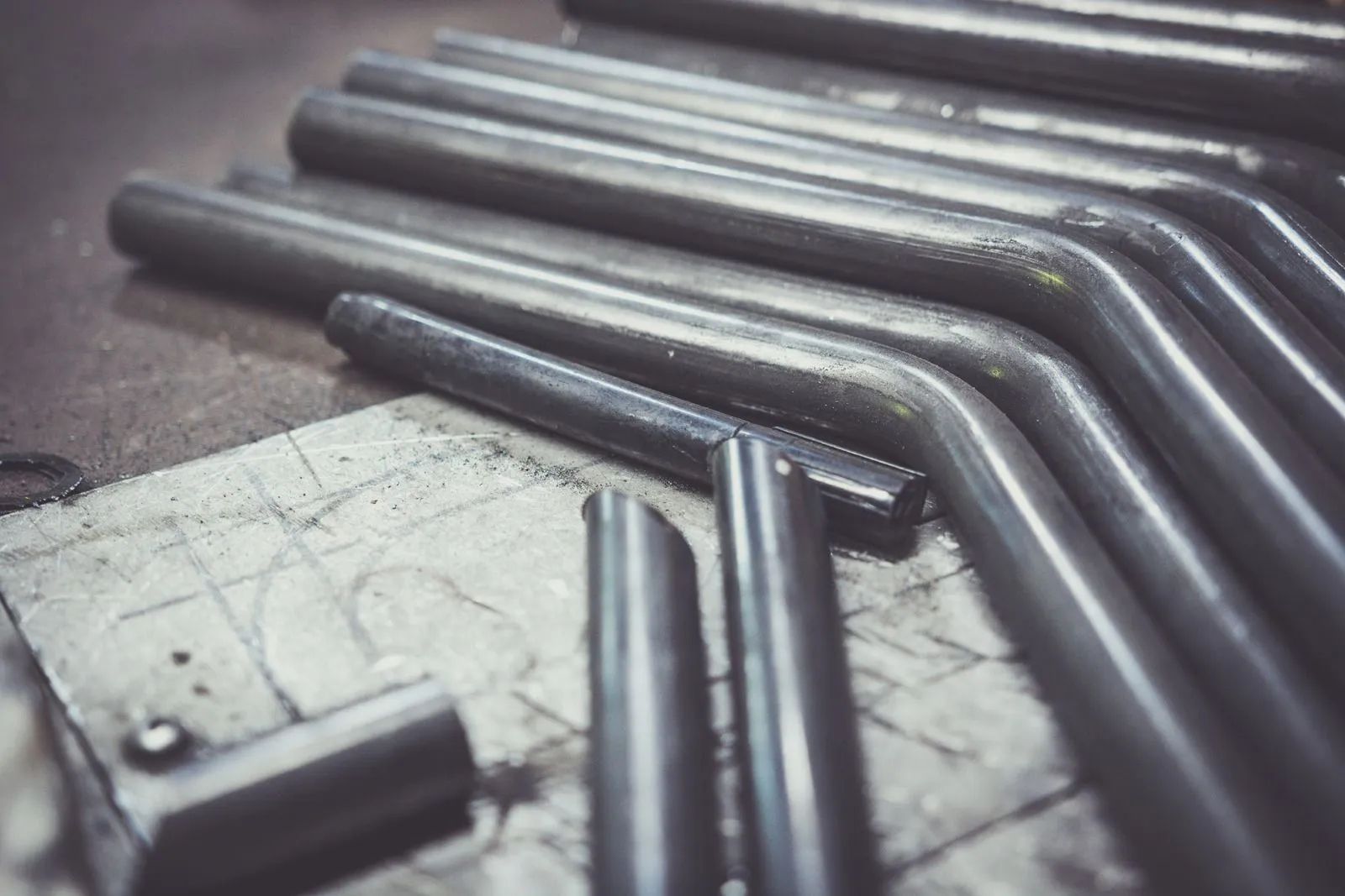 Metal pipes arranged in a zigzag pattern on a worn workbench, close-up.