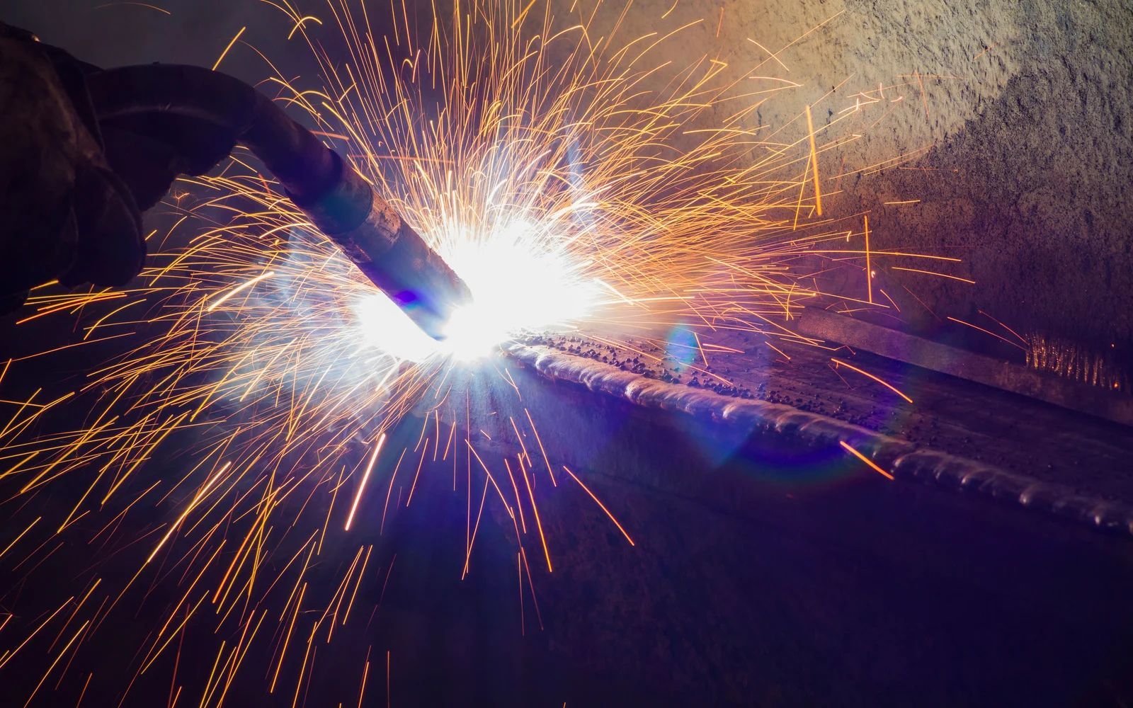 Person welding metal, creating bright orange sparks in a dark workshop.