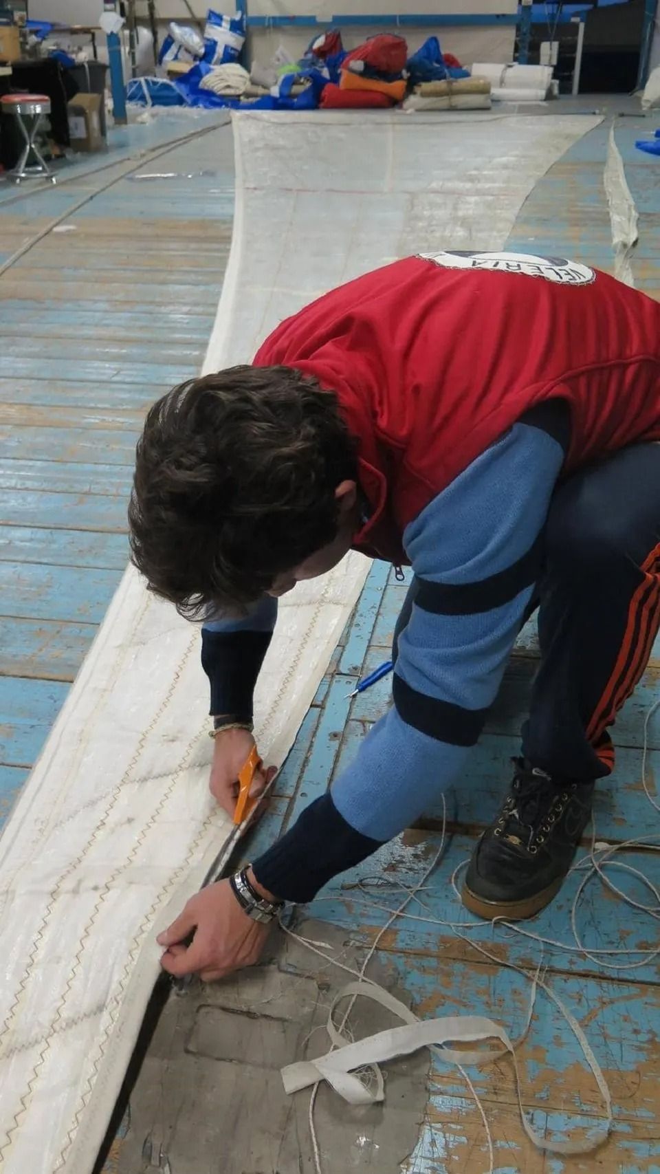 Una persona con una giacca rossa taglia un telo di stoffa bianca sul pavimento blu di un'officina.
