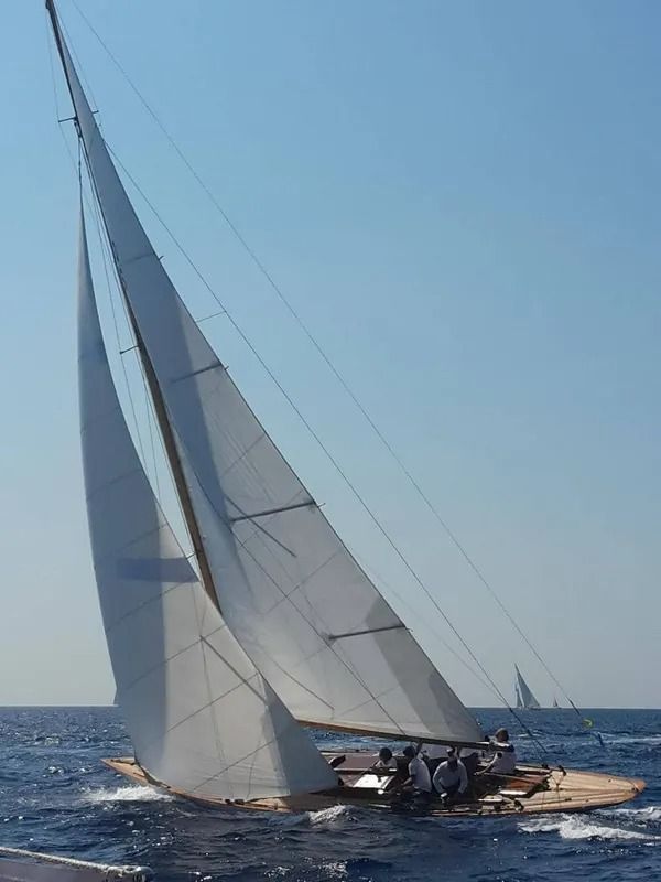 Una barca a vela che naviga in mare in una giornata di sole, con le vele spiegate e l'equipaggio visibile.