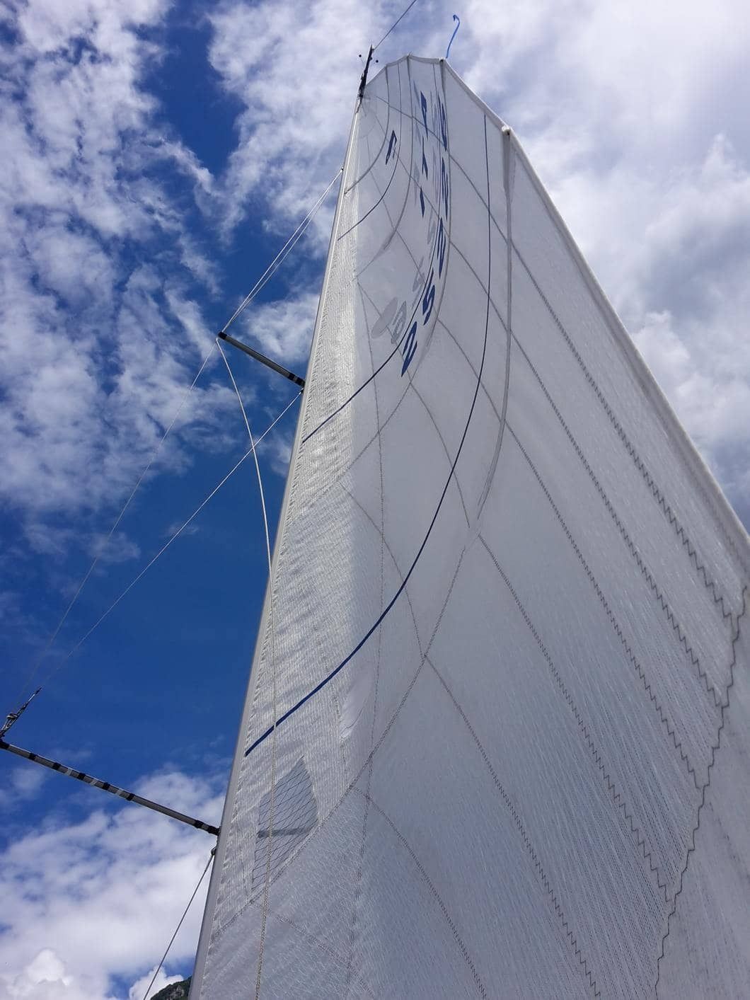 Una barca a vela bianca naviga contro un cielo azzurro con nuvole sparse. La vela è gonfiata dal vento.