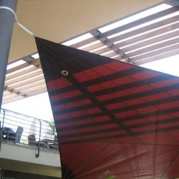 Vela ombreggiante a strisce nere e rosse fissata a una colonna e dotata di tetto a doghe, che fornisce ombra all'esterno.