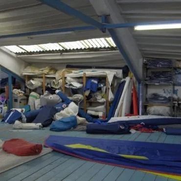 Un'immagine dell'interno di un ripostiglio pieno di vele colorate e piegate, sotto un tetto spiovente.