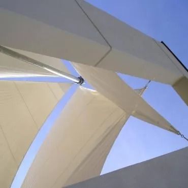 Vele bianche ombreggiate si stagliano contro un cielo azzurro brillante, sostenute da pali e catene di metallo.