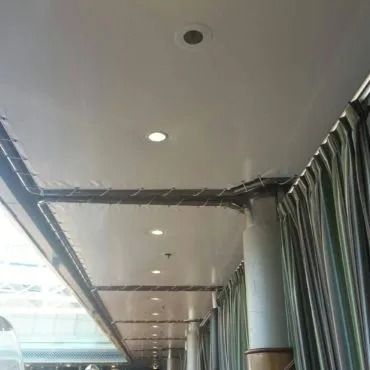 Vista interna di un soffitto bianco con luci incassate, tende lungo un lato e una colonna.