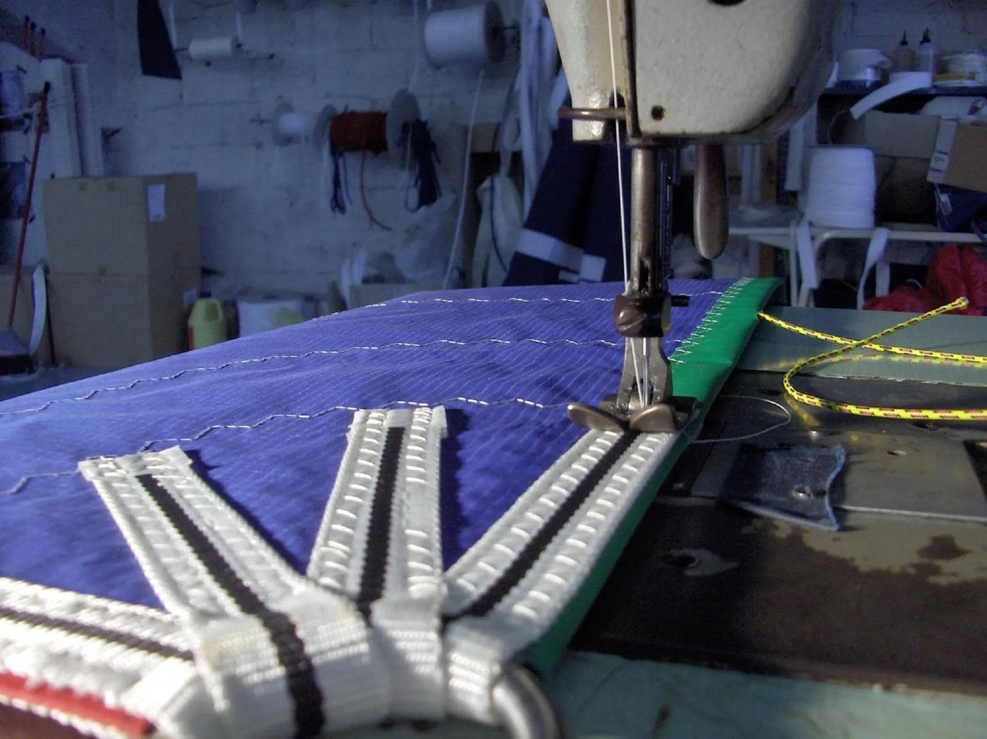 Macchina da cucire che cuce una tela per vele. Primo piano di cinghie bianche e nere cucite su tessuto blu in un laboratorio.