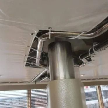 Una colonna di sostegno cilindrica e lucida si estende verso l'alto, circondata da tubi e fili fissati a un soffitto bianco.