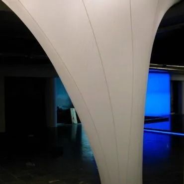 Pilastro bianco e curvo in uno spazio interno; sullo sfondo è visibile uno schermo blu.
