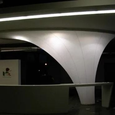 Moderna reception bianca con soffitto curvo e illuminato, inserita in uno spazio scarsamente illuminato.