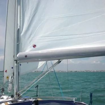 Barca a vela in acqua con la vela issata, cielo azzurro e acqua limpida.