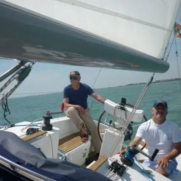 Due uomini navigano su una barca a vela in una giornata di sole. Uno è al timone, mentre l'altro è seduto lì vicino.