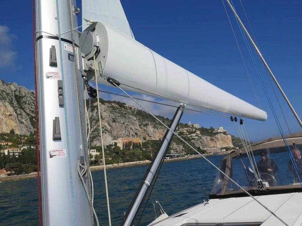 Barca a vela con albero e boma bianchi, che naviga sulle acque blu con la costa sullo sfondo.