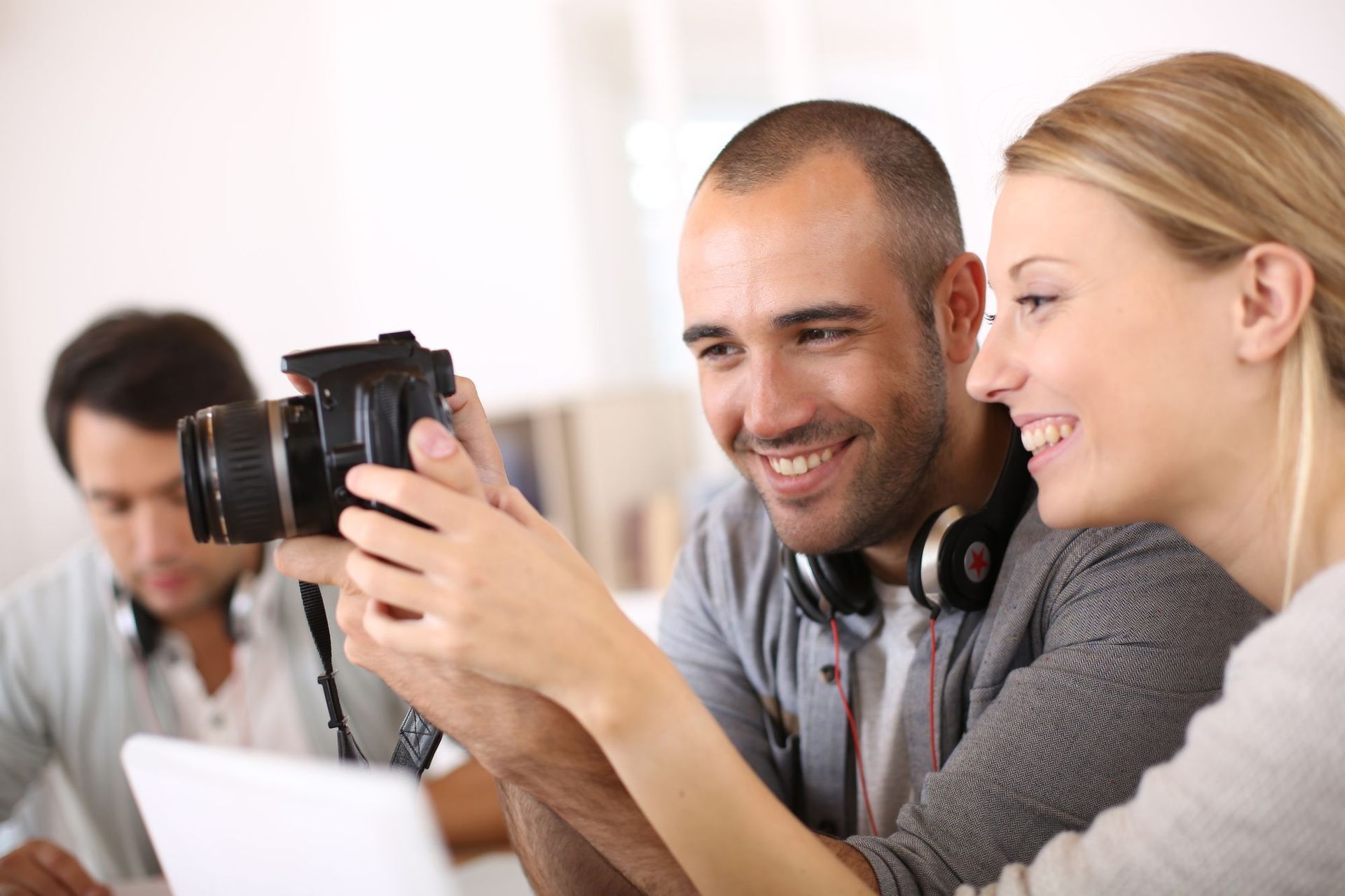 Three coworkers smiling as they view a camera together in a bright office