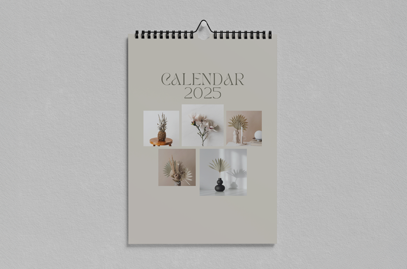 Wall calendar with a beige cover labeled “Calendar 2025” and small botanical photos hanging on a wall.