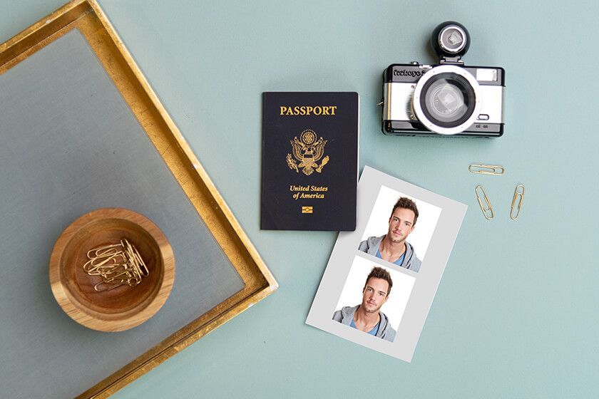 Passport, camera, and photo prints on a pale blue desk with a wooden bowl and gold frame.