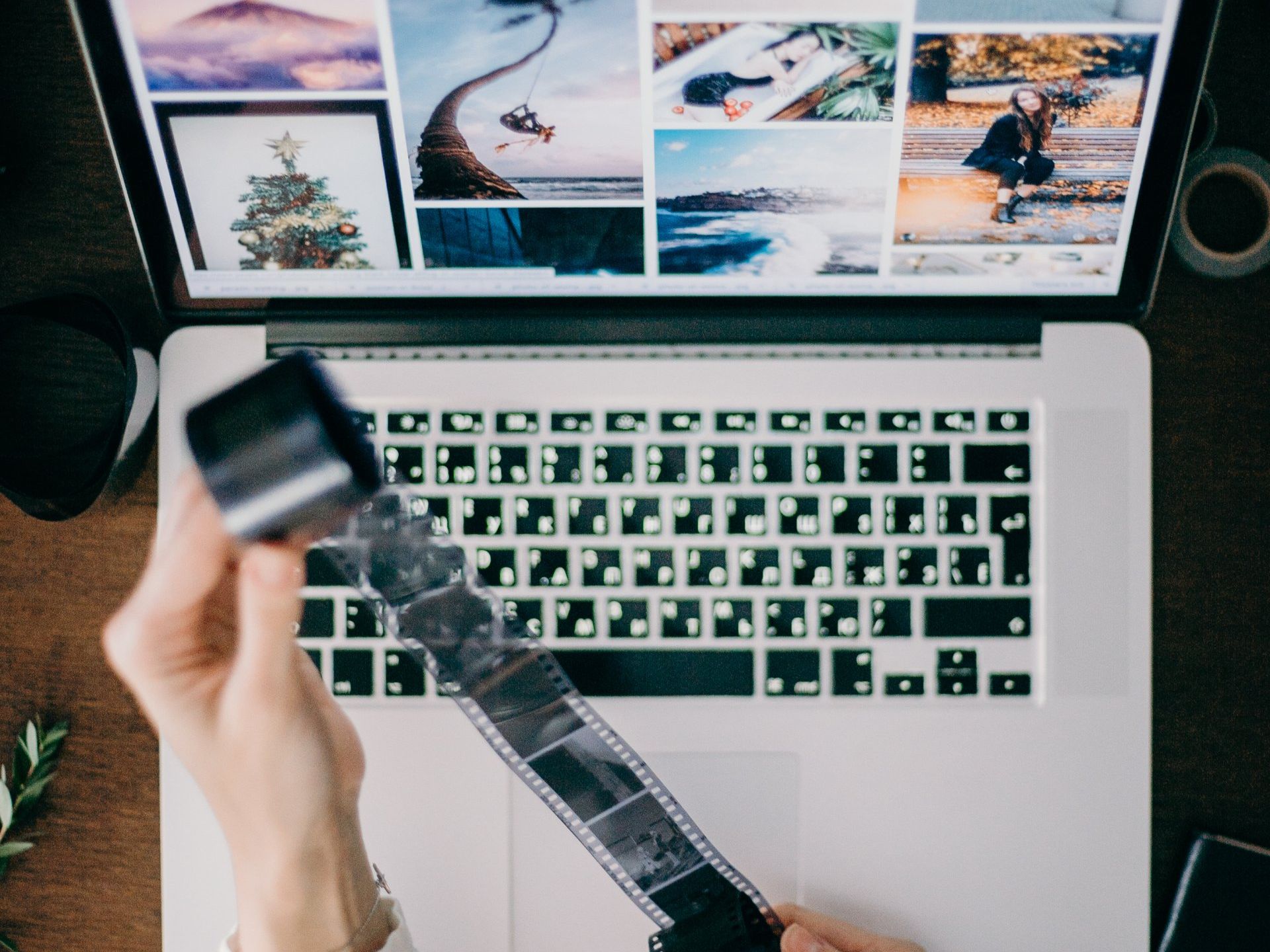 Hands holding film strip over a laptop displaying photos.