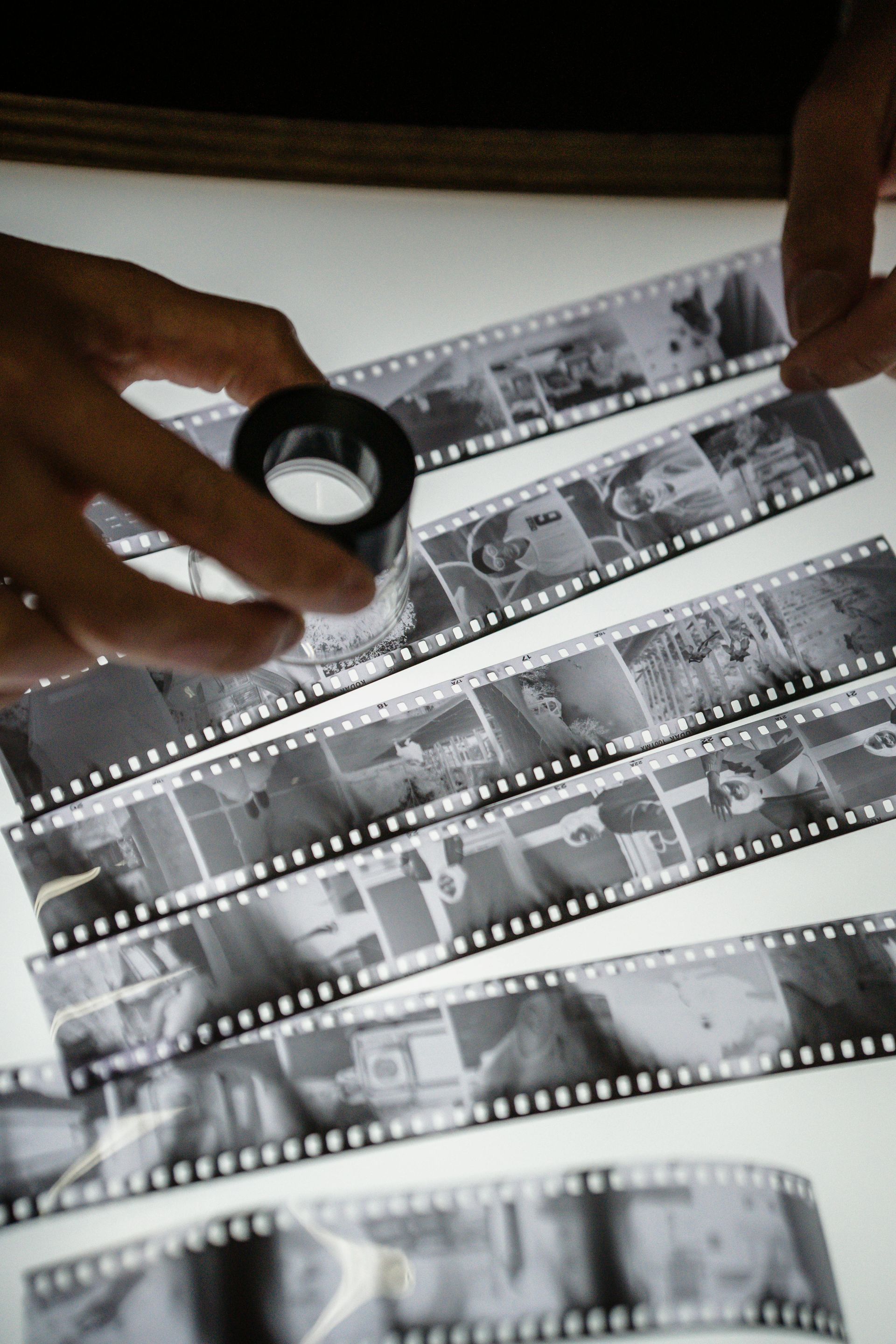 Person examining strips of black and white film with a magnifying glass on a light table.