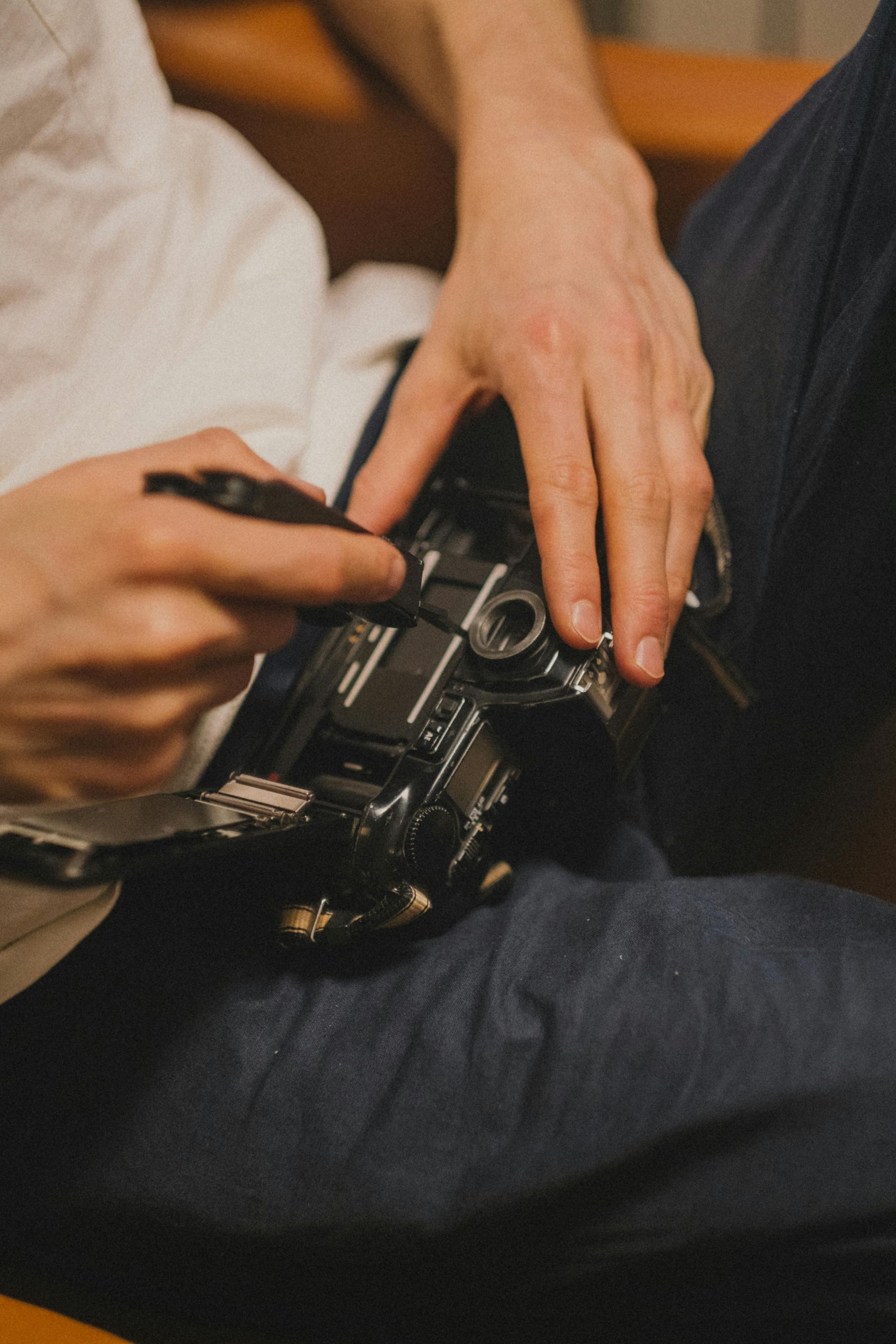 Person holding a camera, working on it with a tool. Wearing a white shirt and blue pants.