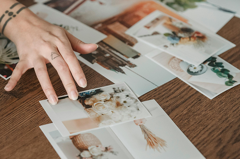 Hand with triangle tattoo points to photographs scattered on a wooden table.